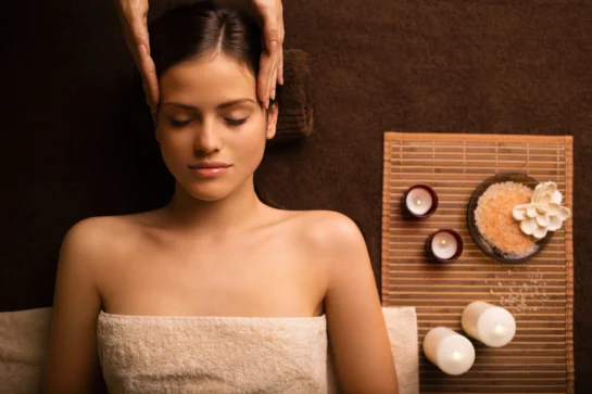 Como fazer marketing para massagens: 7 estratégias para divulgar os serviços 1 Mulher relaxando durante uma massagem com velas e itens de spa. É uma imagem utilizada em marketing para massagens.