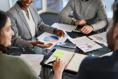 Grupo de pessoas em reunião analisando gráficos coloridos e documentos sobre o que é planejamento financeiro empresarial.