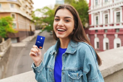 Mulher sorri, de jaqueta e blusa azul, mostrando que existem diferentes bandeiras de cartão de crédito, como a do cartão Asaas.