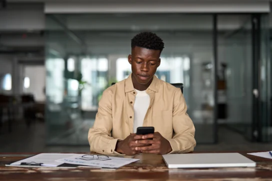 Homem usando celular em escritório, sugerindo consulta ao limite do Pix ou transações financeiras durante o trabalho.