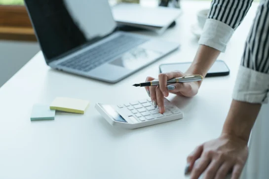 Como precificar o valor da mensalidade escolar corretamente e evitar inadimplência 1 Mulher calculando despesas mensais com uma calculadora, representando a gestão da mensalidade escolar.
