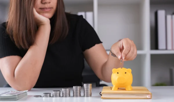 7 maneiras infalíveis de como conquistar a independência financeira 1 mulher colocando dinheiro em cofre e aprendendo como conquistar a independência financeira.