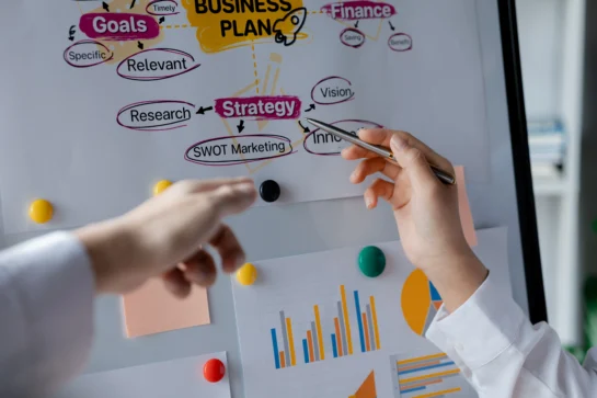 4 dicas de como fazer planejamento empresarial + 6 ferramentas gratuitas 1 Pessoa apontando para diversos termos em um fluxograma, como Marketing, Estratégia, etc., que fazem parte de como fazer planejamento empresarial.