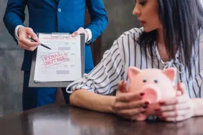 Mulher assustada segura um cofre de porquinho enquanto um homem aponta para um aviso de despejo. Saber o prazo para protestar boleto vencido pode ser essencial para evitar situações como essa.