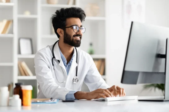 Perdeu o prazo para declarar a DMED? Saiba o que fazer! 1 Médico digitando no computador em consultório, ilustrando uso da DMED, documento utilizado para prestar contas à Receita Federal.