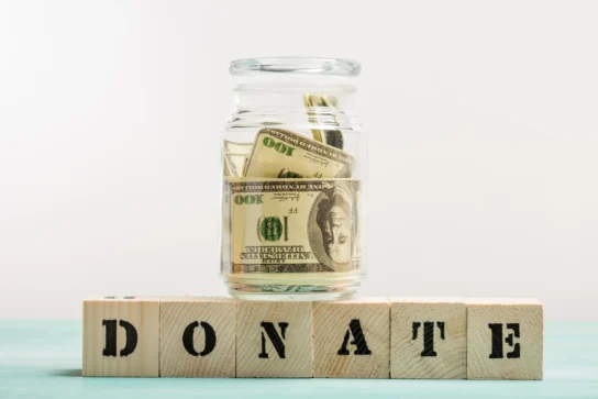 Como declarar doação recebida: entenda quem precisa declarar 1 Pote com dólares e blocos escrito "Donate", representando como declarar doação recebida na declaração de imposto de renda.